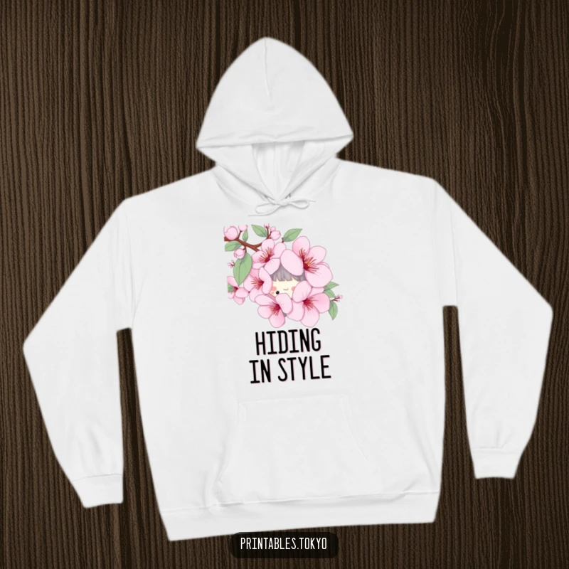 Funny hoodie with a playful character peeking from behind a stylized cherry blossom, offering cozy spring vibes.